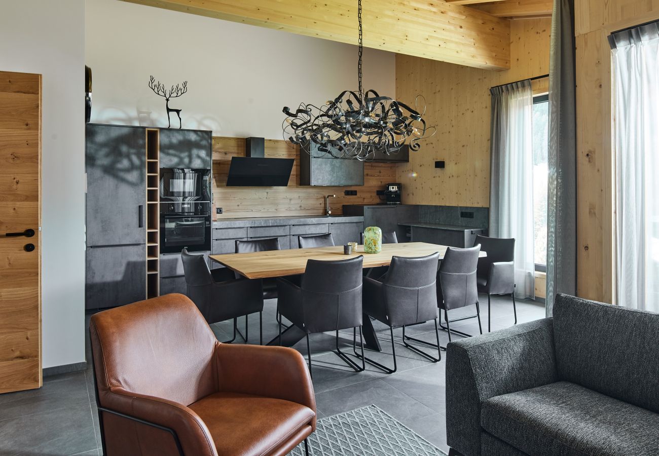 Woonkamer met keuken, tafel, 8 stoelen, een bank en een fauteuil in Alm Lodge 3